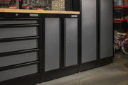 A close-up view of CRAFTSMAN storage cabinets and drawers with a wood countertop in a garage or workshop setting. The cabinets have a sleek black and gray finish.